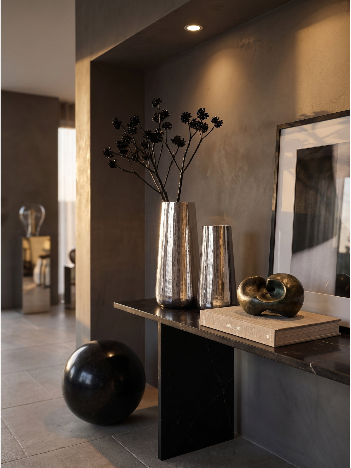 Die 45 cm hohe silberne Deko-Vase mit einem schwarzen Mitsumata-Zweig neben einer Bronzeskulptur auf einer minimalistischen Anrichte._