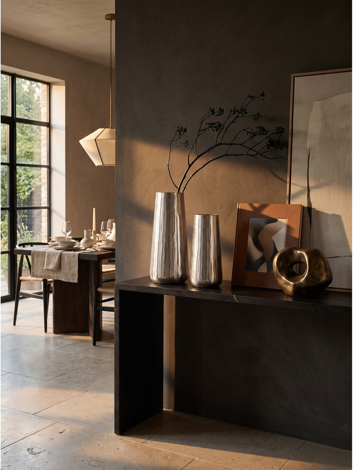 Zweiteiliges Vasen-Set aus Aluminium arrangiert auf einem schwarzen Sideboard vor einer fugenlosen grauen Wand auf Kalksteinboden.