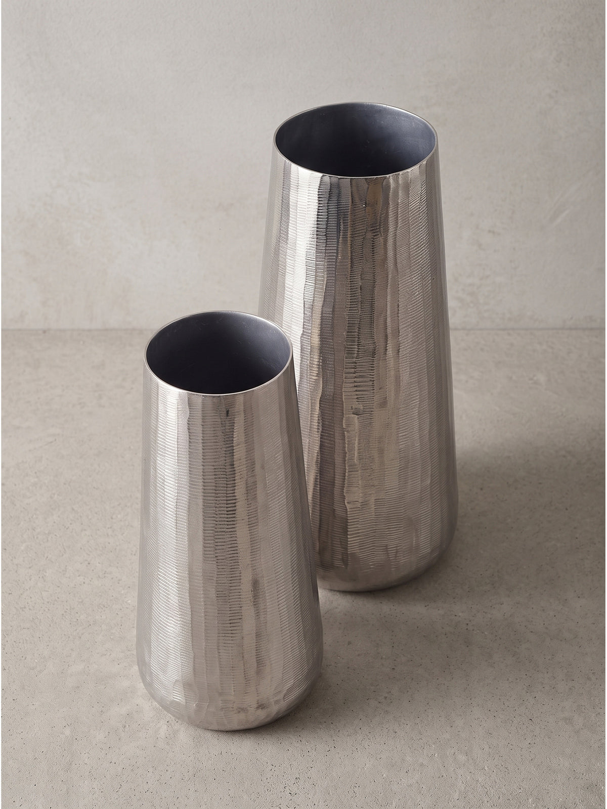 Leicht versetzte Ansicht der beiden modernen Metallvasen, die die unregelmäßige reflektierende Oberflächenstruktur des Aluminiums zeigt._