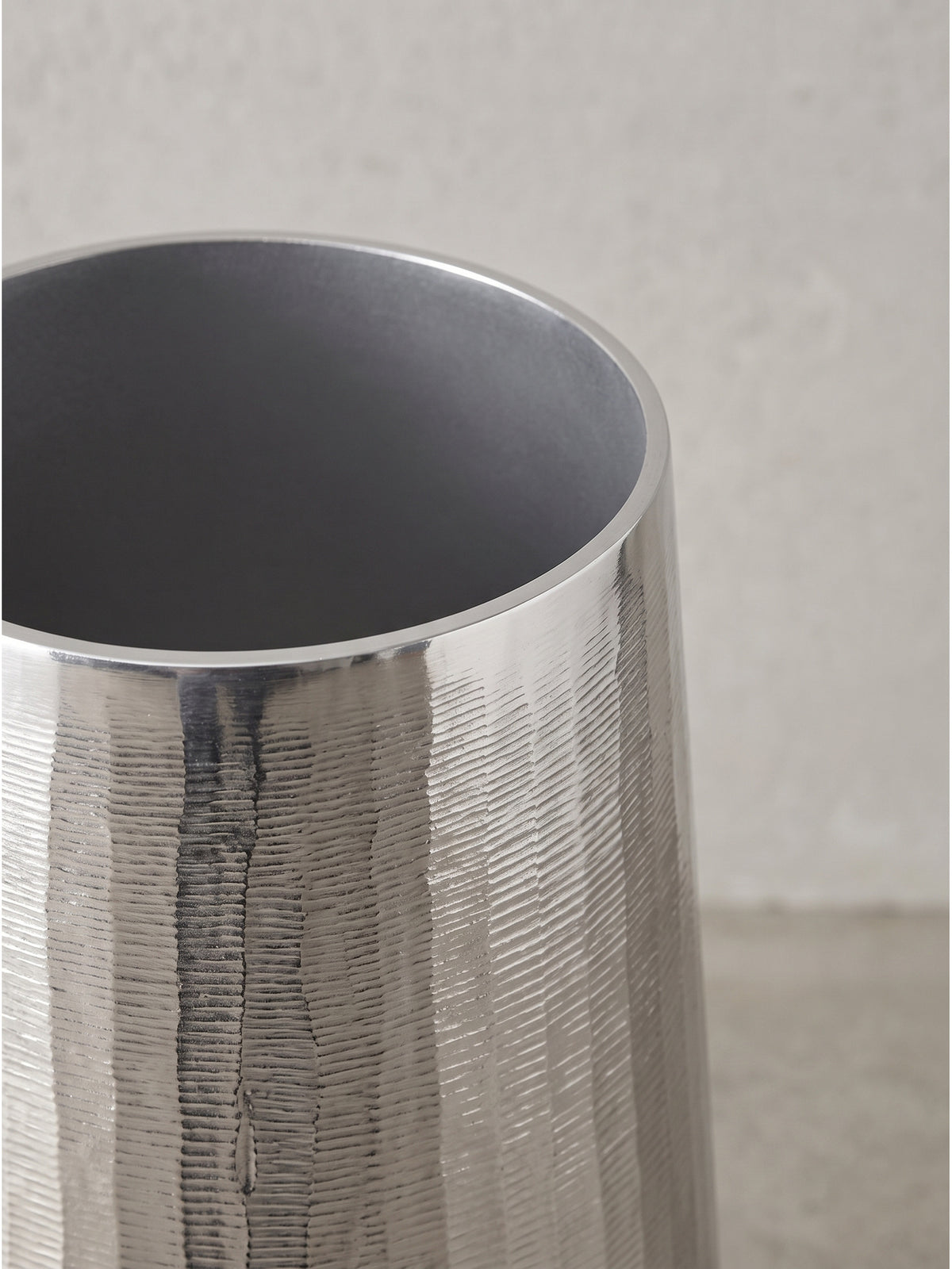 Kühle metallische Lichtreflexe auf der strukturierten Oberfläche der handgefertigten Deko-Vasen aus silbernem Aluminium._