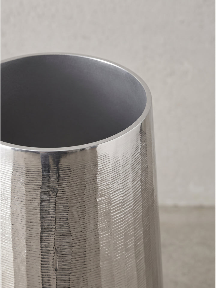 Kühle metallische Lichtreflexe auf der strukturierten Oberfläche der handgefertigten Deko-Vasen aus silbernem Aluminium._