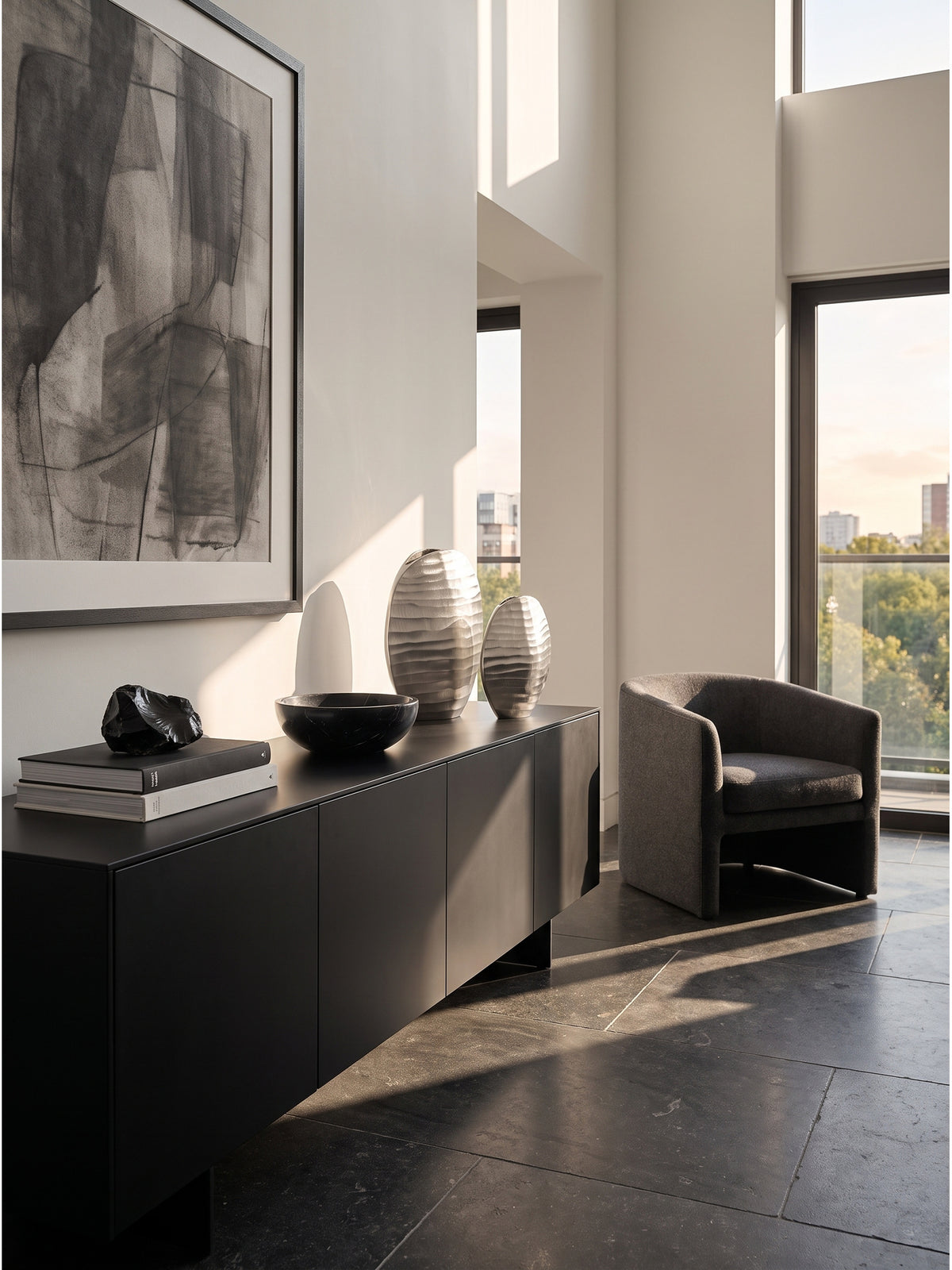 Großzügiges modernes Wohnzimmer mit einem skulpturalen 2er Set Aluminium Vasen in Silber auf einem mattschwarzen Sideboard._