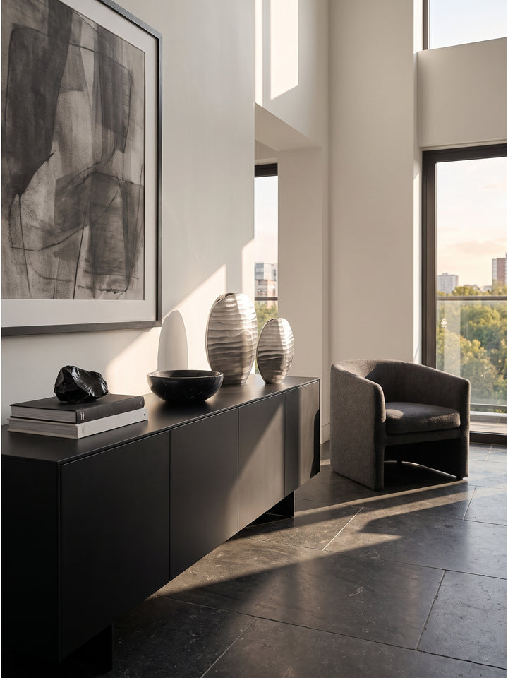 Großzügiges modernes Wohnzimmer mit einem skulpturalen 2er Set Aluminium Vasen in Silber auf einem mattschwarzen Sideboard._