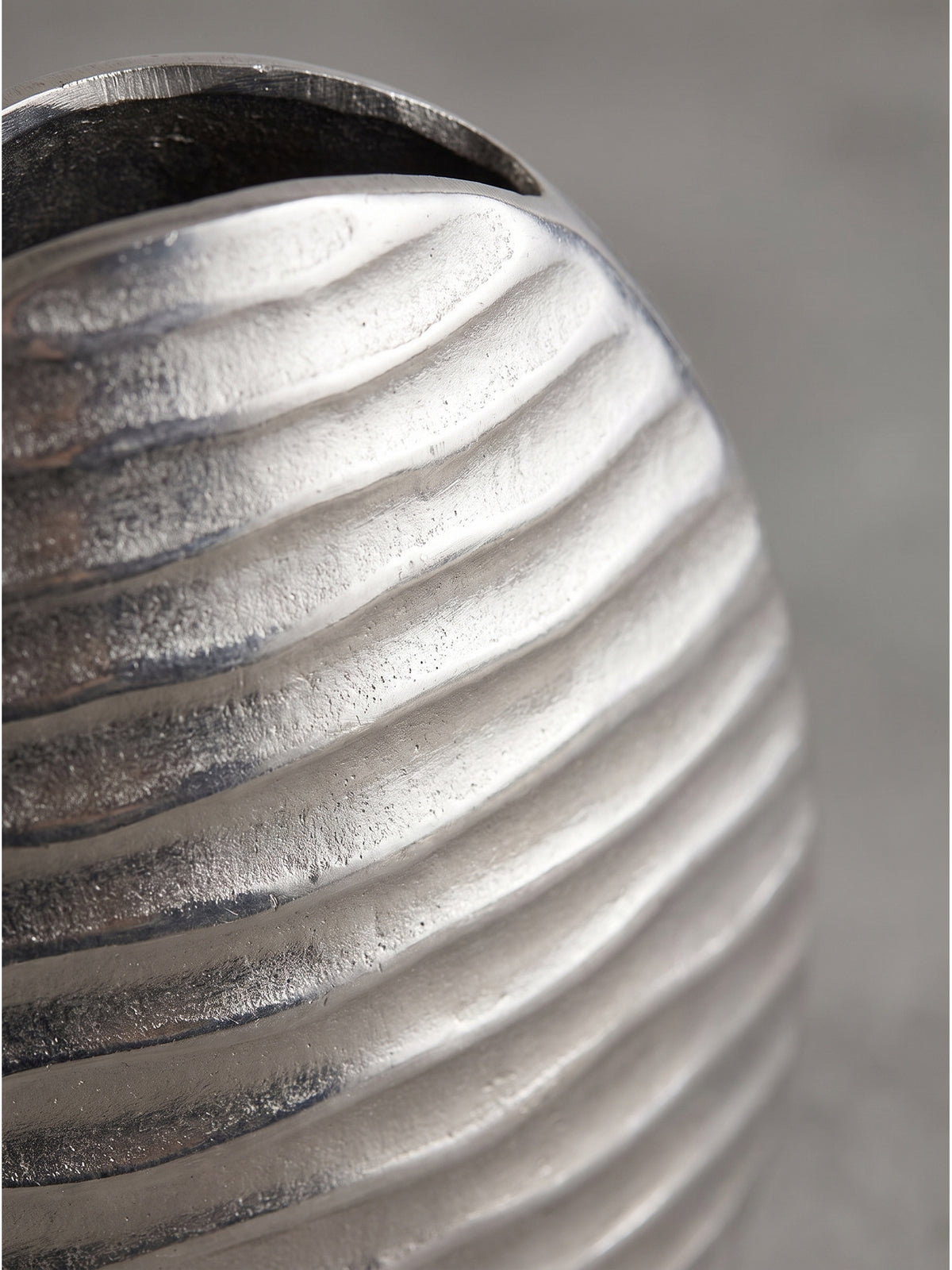 Detaillierte Nahaufnahme der wellenförmigen Oberflächenstruktur der silber lackierten Aluminiumvase im hellen Tageslicht._