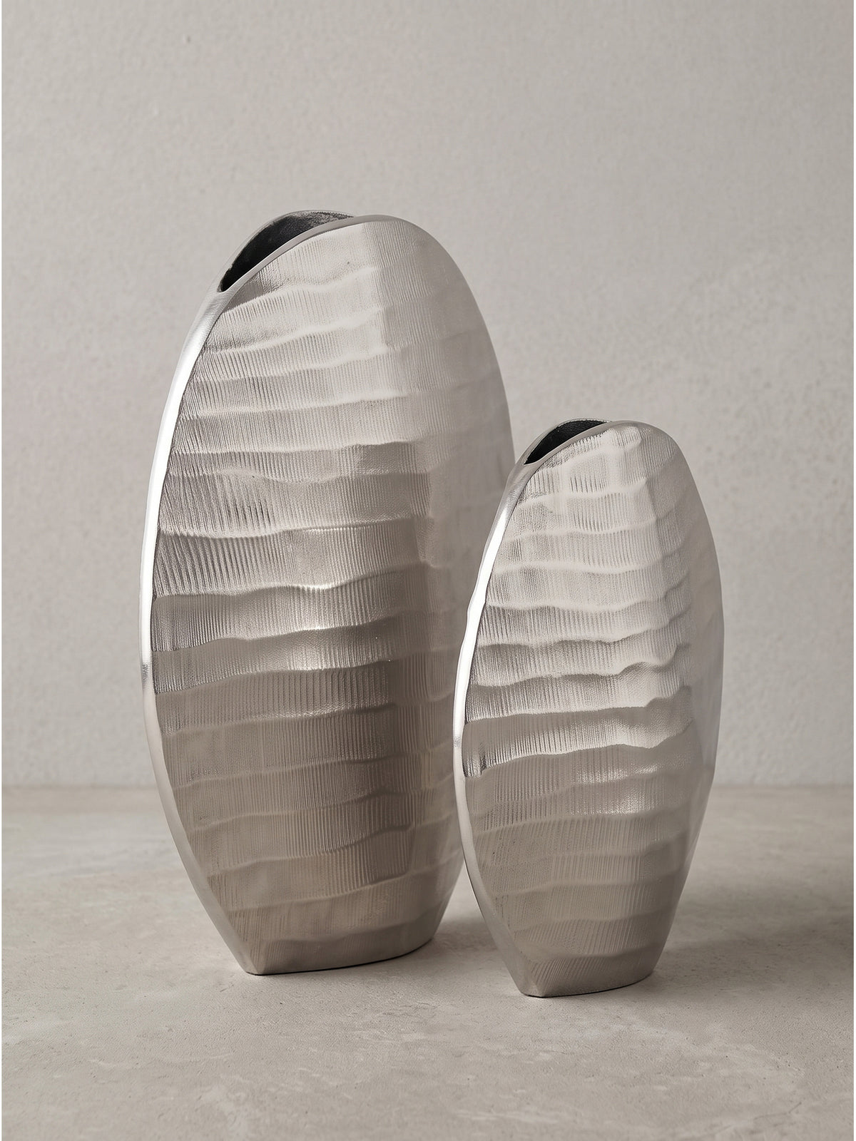 Die schmale, elliptische Form der handgearbeitet wirkenden Aluminiumvasen in der seitlichen Detailansicht._