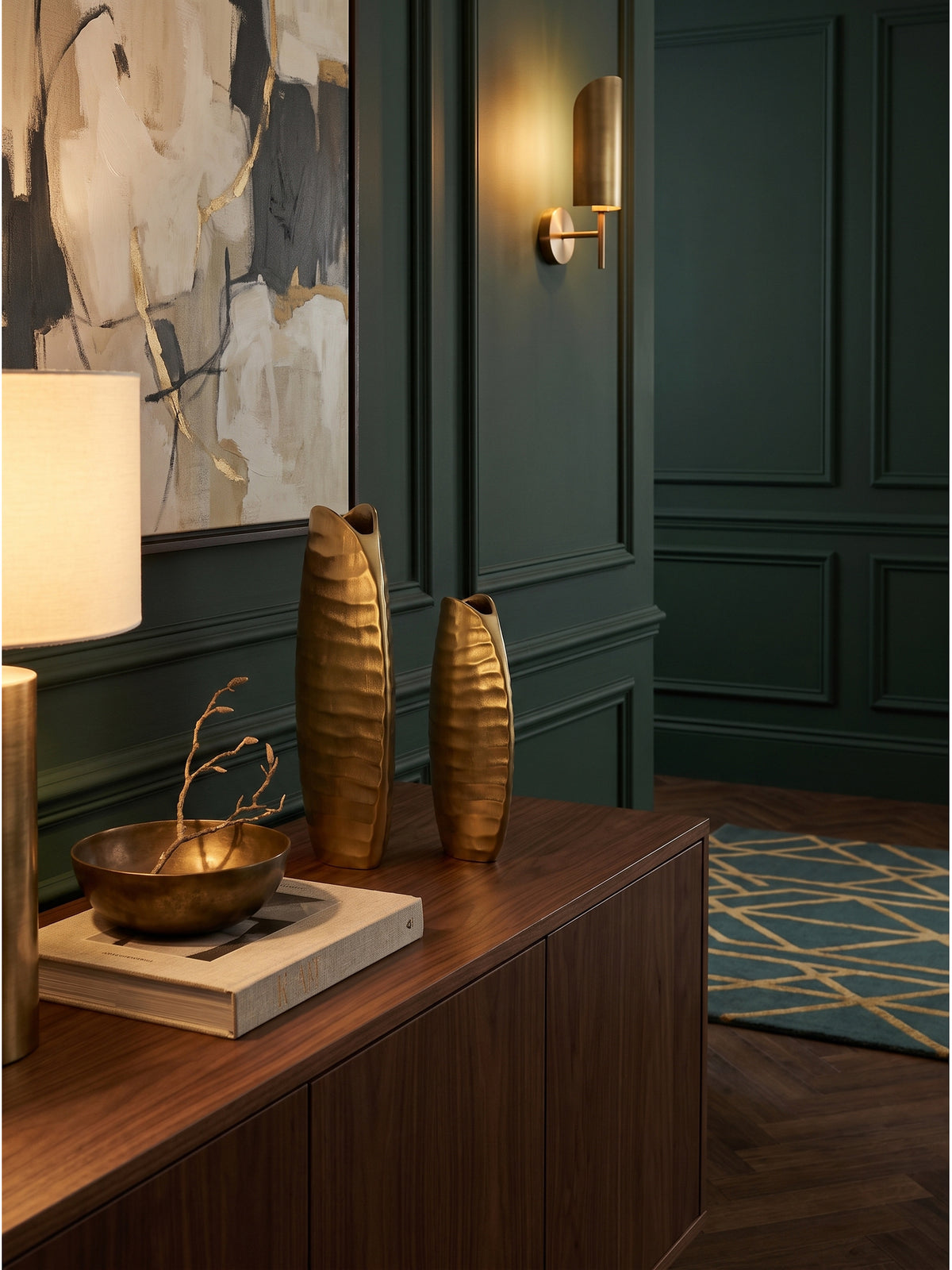 Die kleine goldene Alu Tischvase dekoriert mit einem getrockneten Weidenzweig auf einem Holzsideboard im Art-Deco Wohnzimmer._
