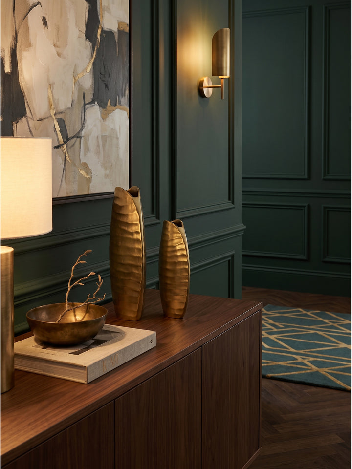 Die kleine goldene Alu Tischvase dekoriert mit einem getrockneten Weidenzweig auf einem Holzsideboard im Art-Deco Wohnzimmer._