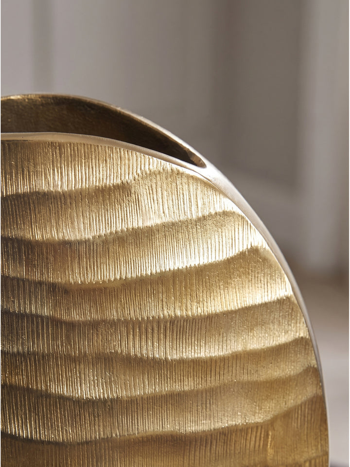 Makroaufnahme der golden lackierten Oberfläche der Aluminiumvase mit markanter horizontaler Rillenstruktur im Licht._