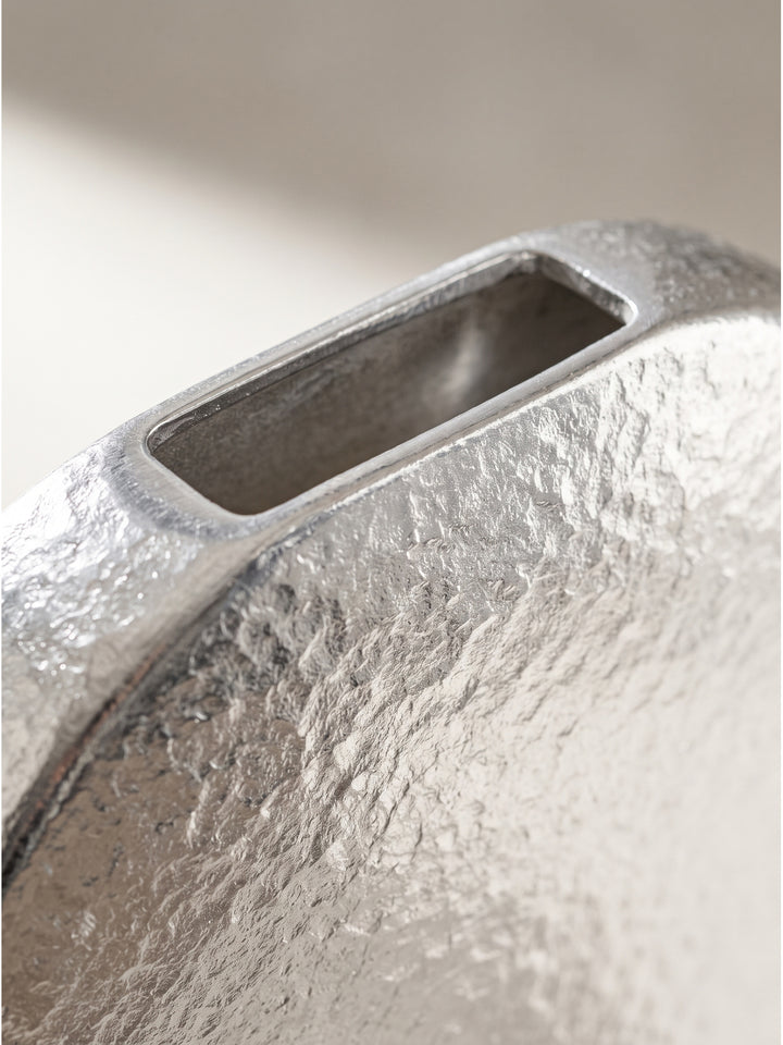 Nahaufnahme der gehämmerten silbernen Aluminiumoberfläche der runden Blumenvase im kühlen Licht._