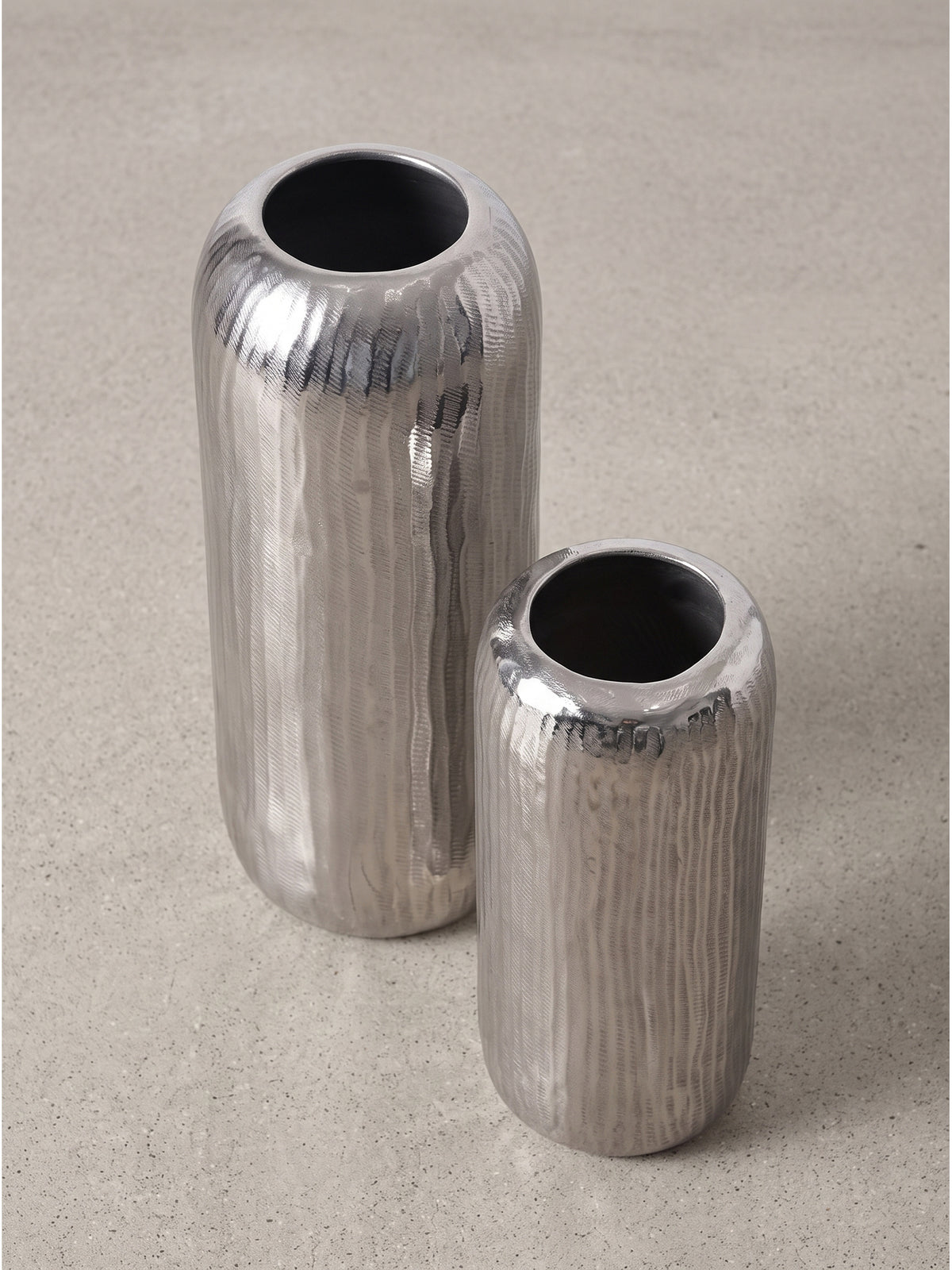 Zweiteiliges Vasenset aus massivem Aluminium mit markantem gehämmertem Finish in seitlicher Studioperspektive._