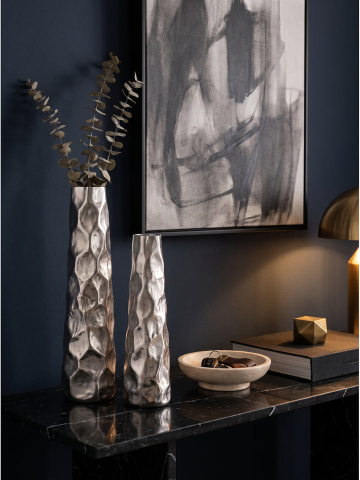 Silberne Blumenvase aus Aluminium mit getrockneten Eukalyptuszweigen neben einem Bildband auf schwarzem Marmor_