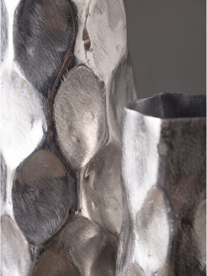 Nahaufnahme der silbernen Aluminium-Oberfläche der Dekovase mit strukturiertem Hammerschlag-Muster und Lichtreflexionen_