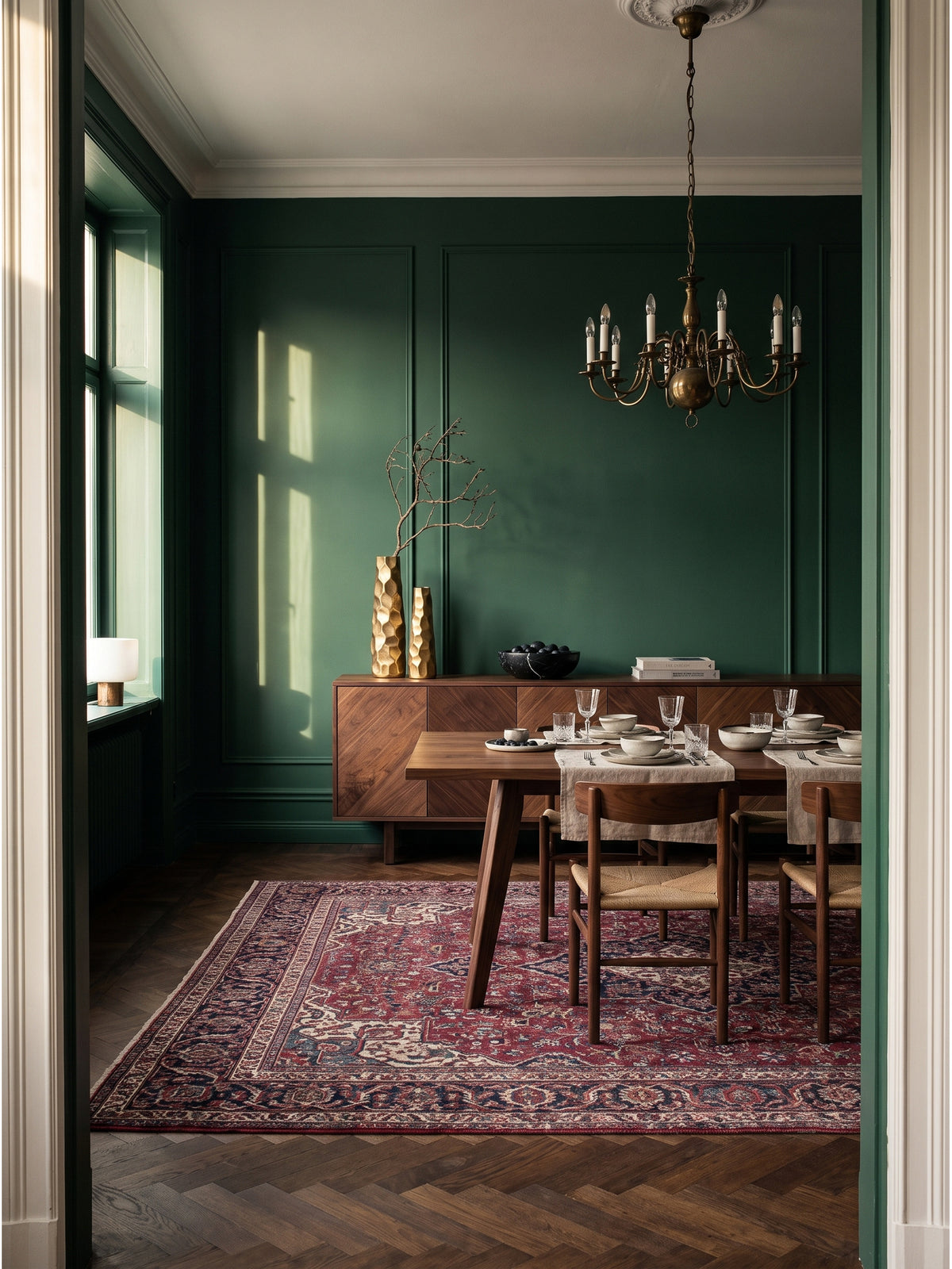 Zwei goldene Dekovasen aus Aluminium mit Hammerschlag-Design auf einer Nussbaum-Anrichte vor einer tiefgrünen Wand im Wohnzimmer
