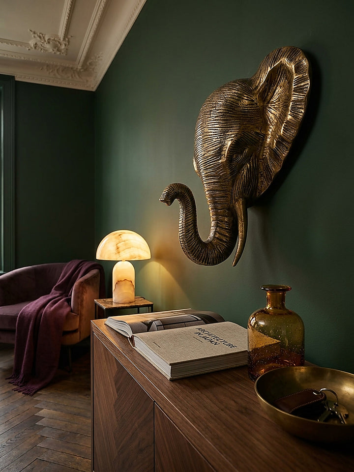 Goldener Elefant als Wandobjekt aus Metall direkt montiert über einem großformatigen Bildband und einem Glas-Dekanter._