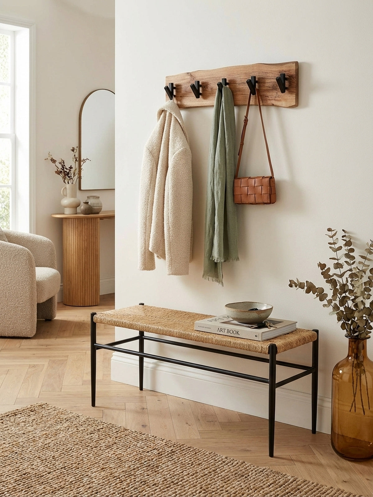 Die Design Wandgarderobe aus Akazienholz mit schwarzen Haken schafft Ordnung in einem hellen, organisch-modernen Eingangsbereich neben einer minimalistischen Sitzbank.