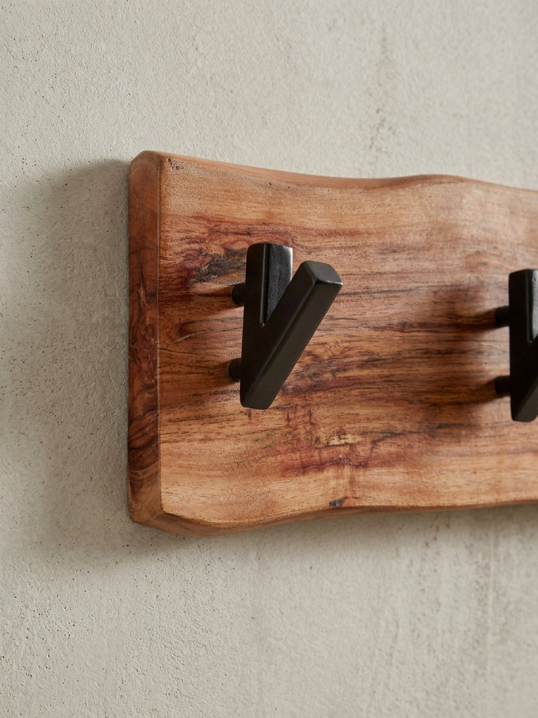 Schräge Perspektive auf die Garderobe aus Akazie Massivholz, die das Zusammenspiel von warmem Holzton und kühlem, schwarzem Metall betont._