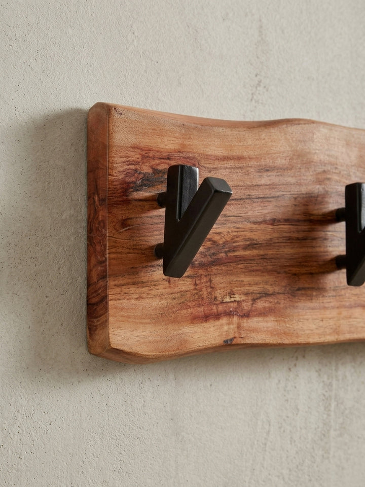 Schräge Perspektive auf die Garderobe aus Akazie Massivholz, die das Zusammenspiel von warmem Holzton und kühlem, schwarzem Metall betont._