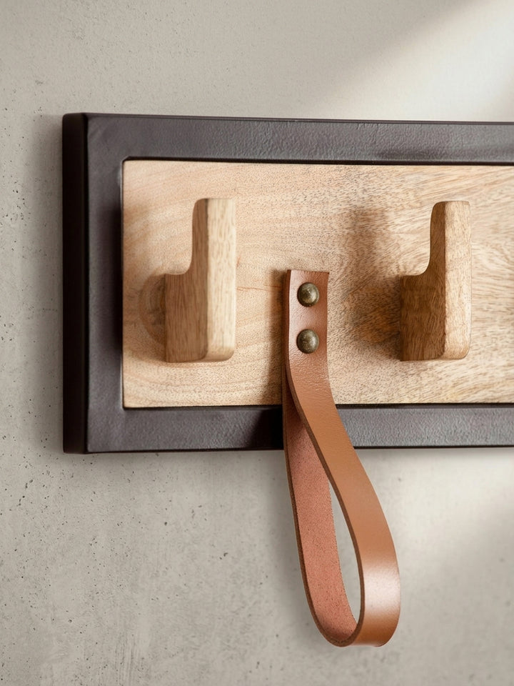 Detailaufnahme eines Nietendetails an einer braunen Lederschlaufe, befestigt an der massiven Mangoholz-Platte der Garderobe._