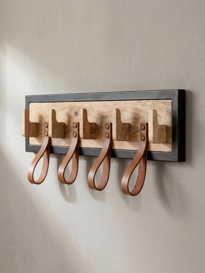 Leicht untersichtige Perspektive der Hakenleiste, die das Zusammenspiel von hellem Mangoholz und dunklem Metallrahmen betont._