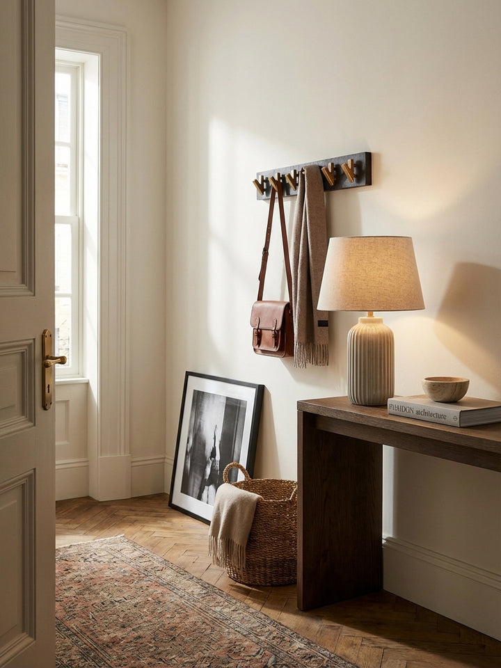 Moderne Wandgarderobe aus schwarzem Mangoholz und Gold in einem eleganten Altbau-Flur mit Fischgrätparkett und einer beigen Wand._