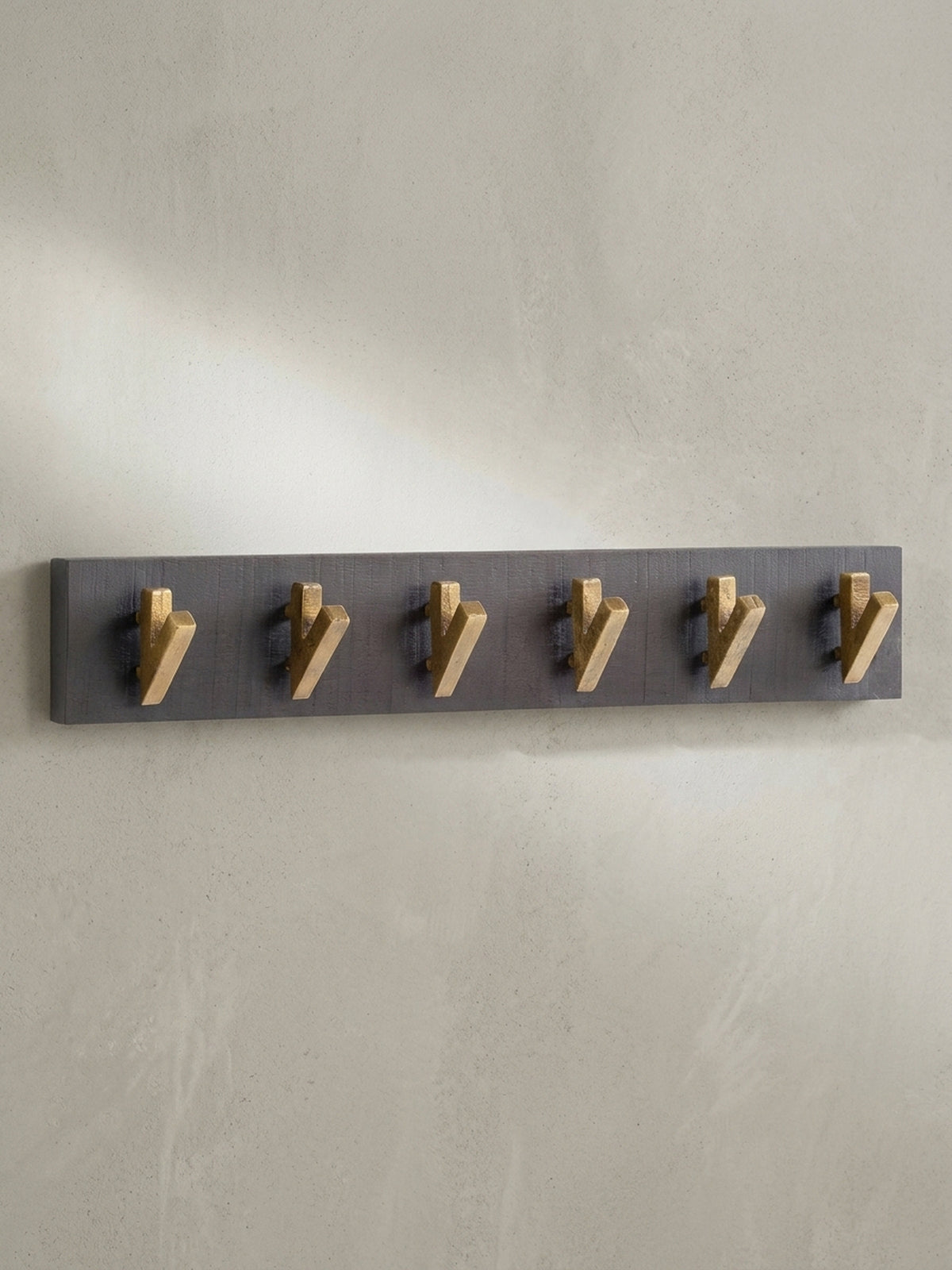 Frontansicht der Wandgarderobe aus massivem Mangoholz in Schwarz mit sechs markanten, V-förmigen Haken aus goldfarbenem Metall.