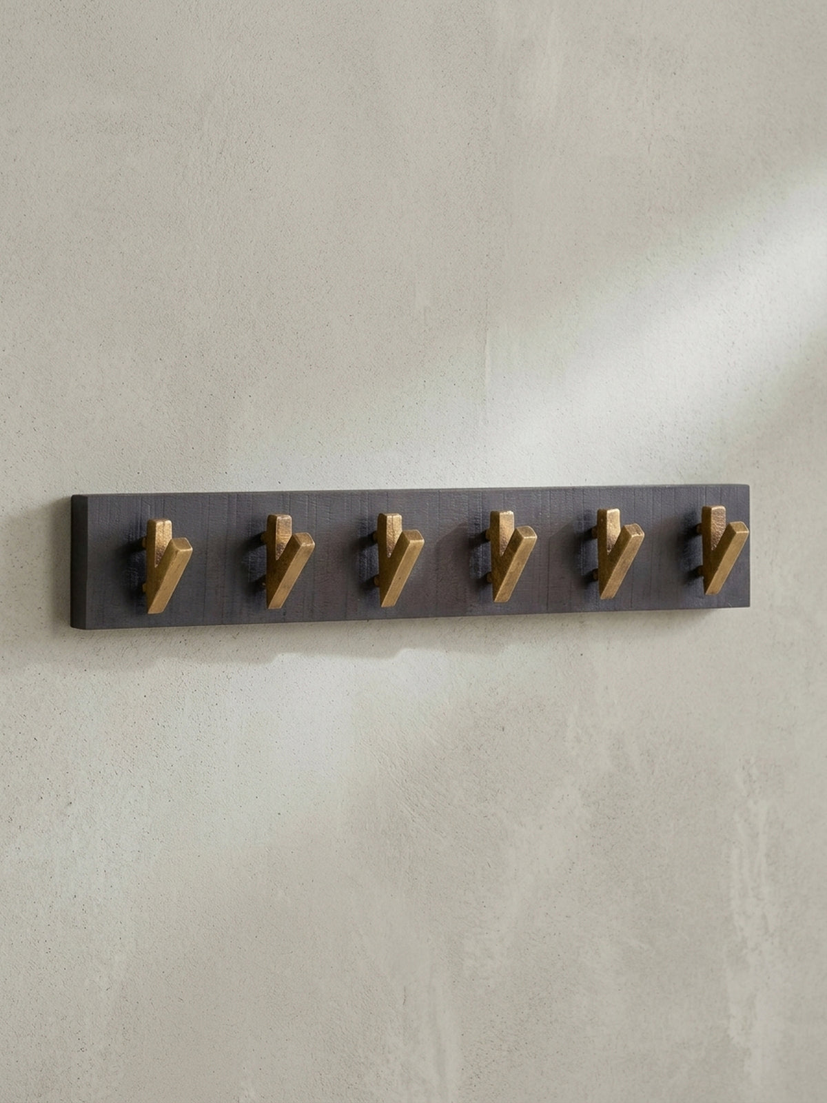 Schräge Ansicht der 60 cm breiten Hakenleiste, die die Tiefe der goldenen Metallhaken vor der schwarzen Holzleiste zeigt.