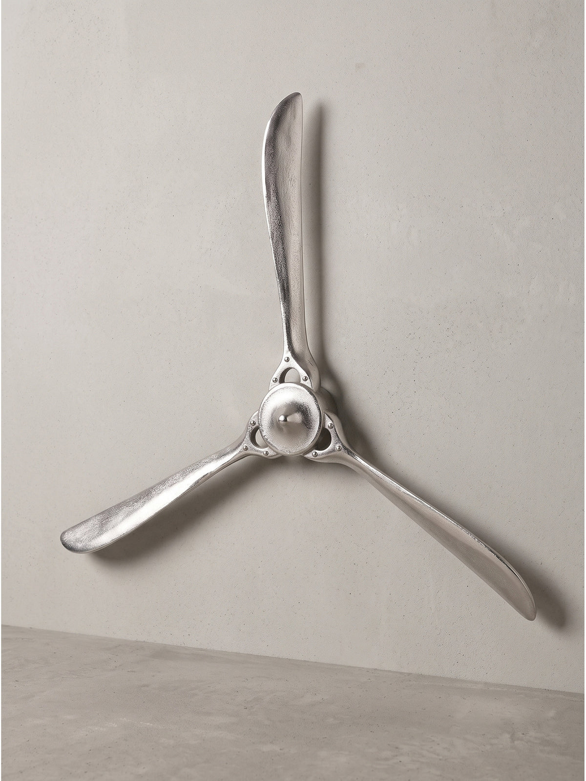 Frontale Perspektive des silbernen Flugzeugpropellers vor dunklem Hintergrund, welche die detaillierte Nabe mit Nietenoptik hervorhebt._
