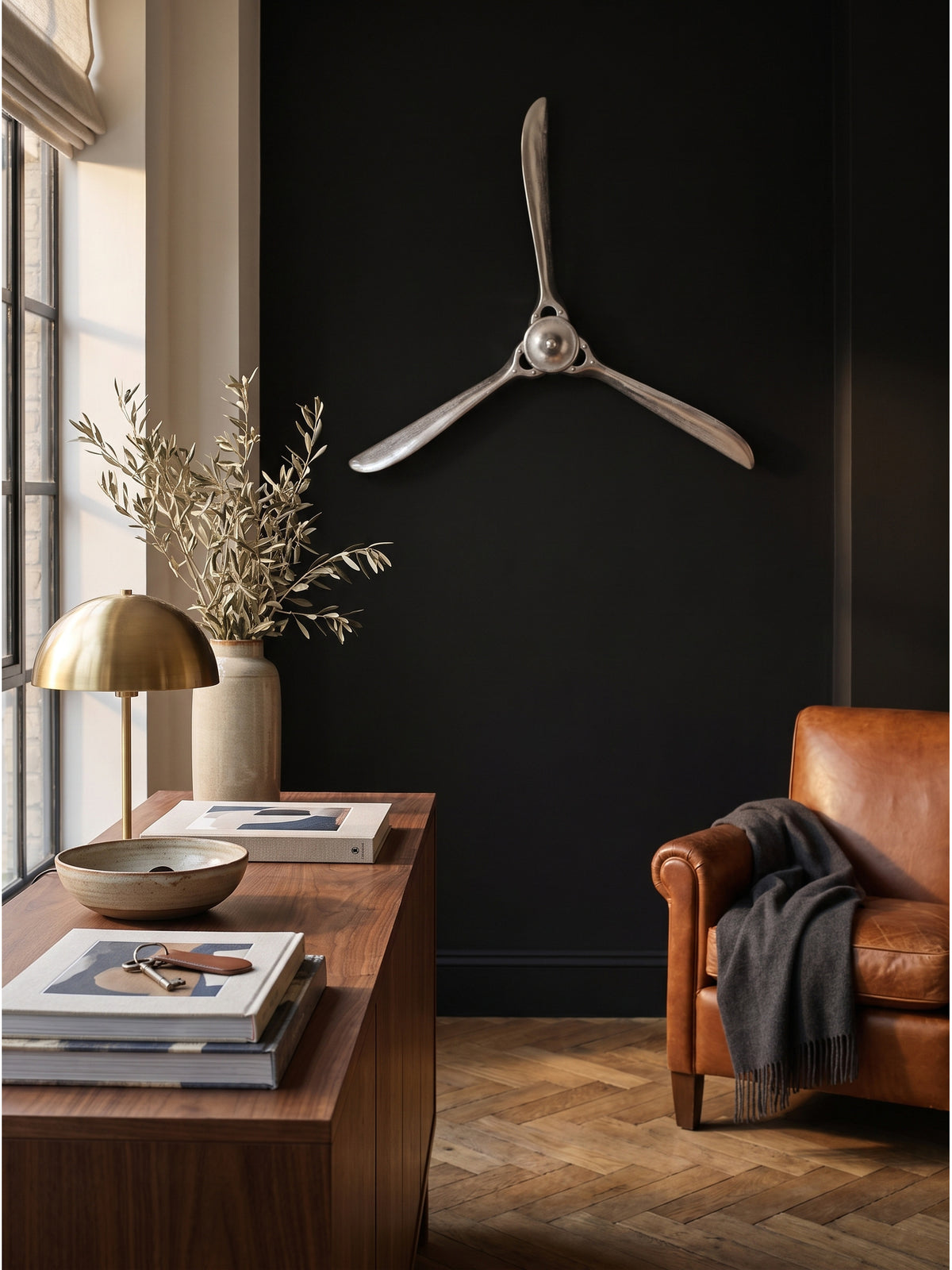 Dreiblättriger Deko Propeller an der Wand eines Arbeitszimmers arrangiert über einem Stapel alter Fotobände und einer Marmorschale._