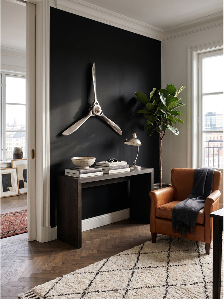 Silberner Wandpropeller aus Aluminium im Ensemble mit einem cognacfarbenen Ledersessel und einer schwarzen Stahl-Stehleuchte im Raum._