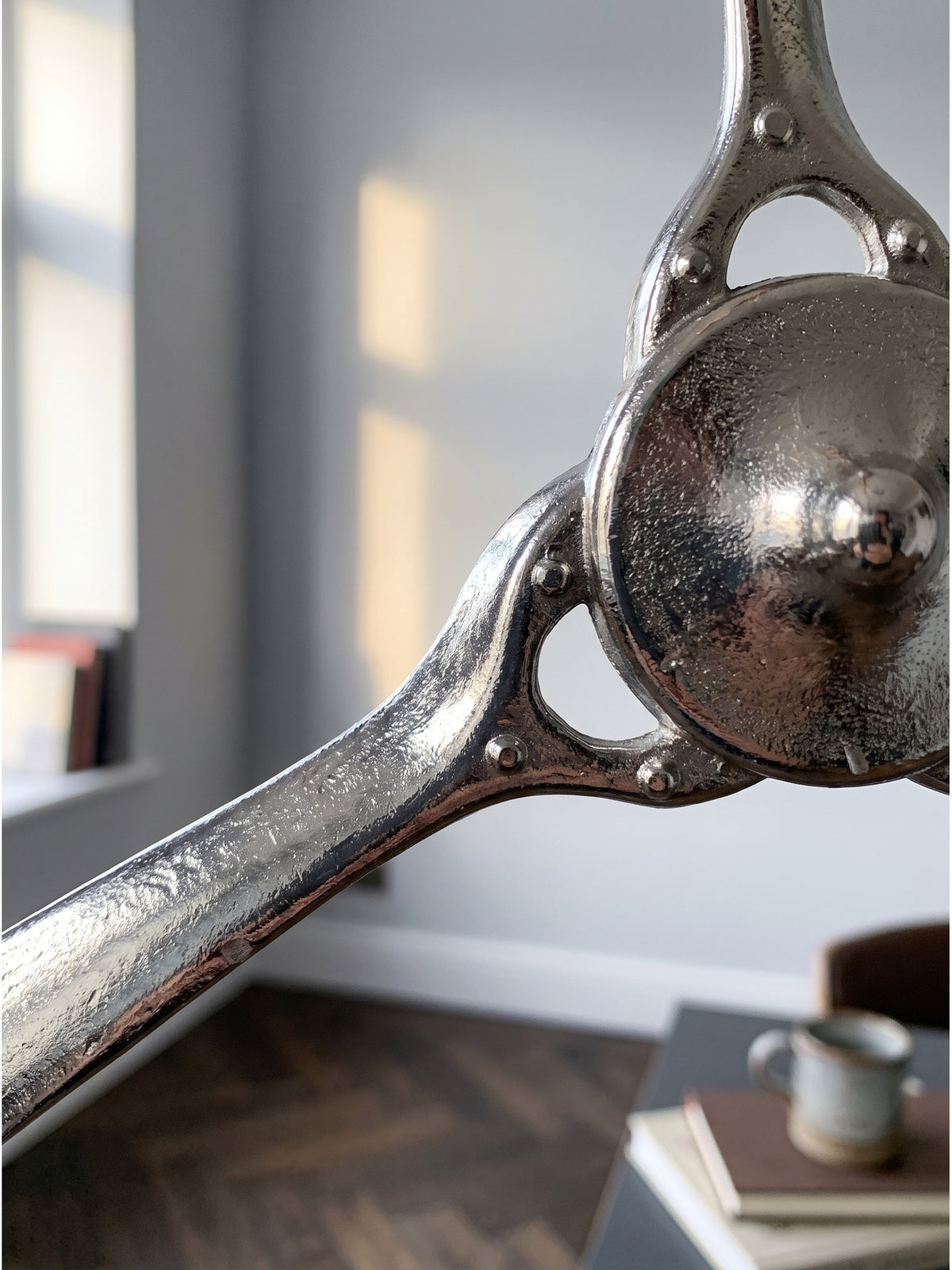 Nahaufnahme der kühlen Aluminiumoberfläche des silbernen Wandpropellers mit sichtbarer Lichtreflexion auf den geschwungenen Blättern.