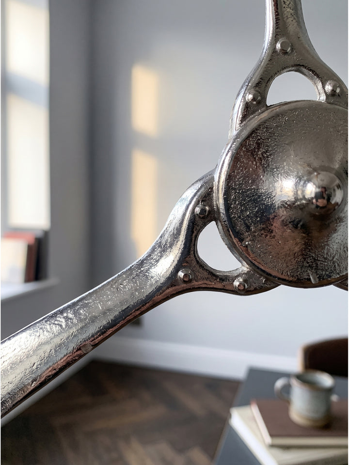 Nahaufnahme der kühlen Aluminiumoberfläche des silbernen Wandpropellers mit sichtbarer Lichtreflexion auf den geschwungenen Blättern._
