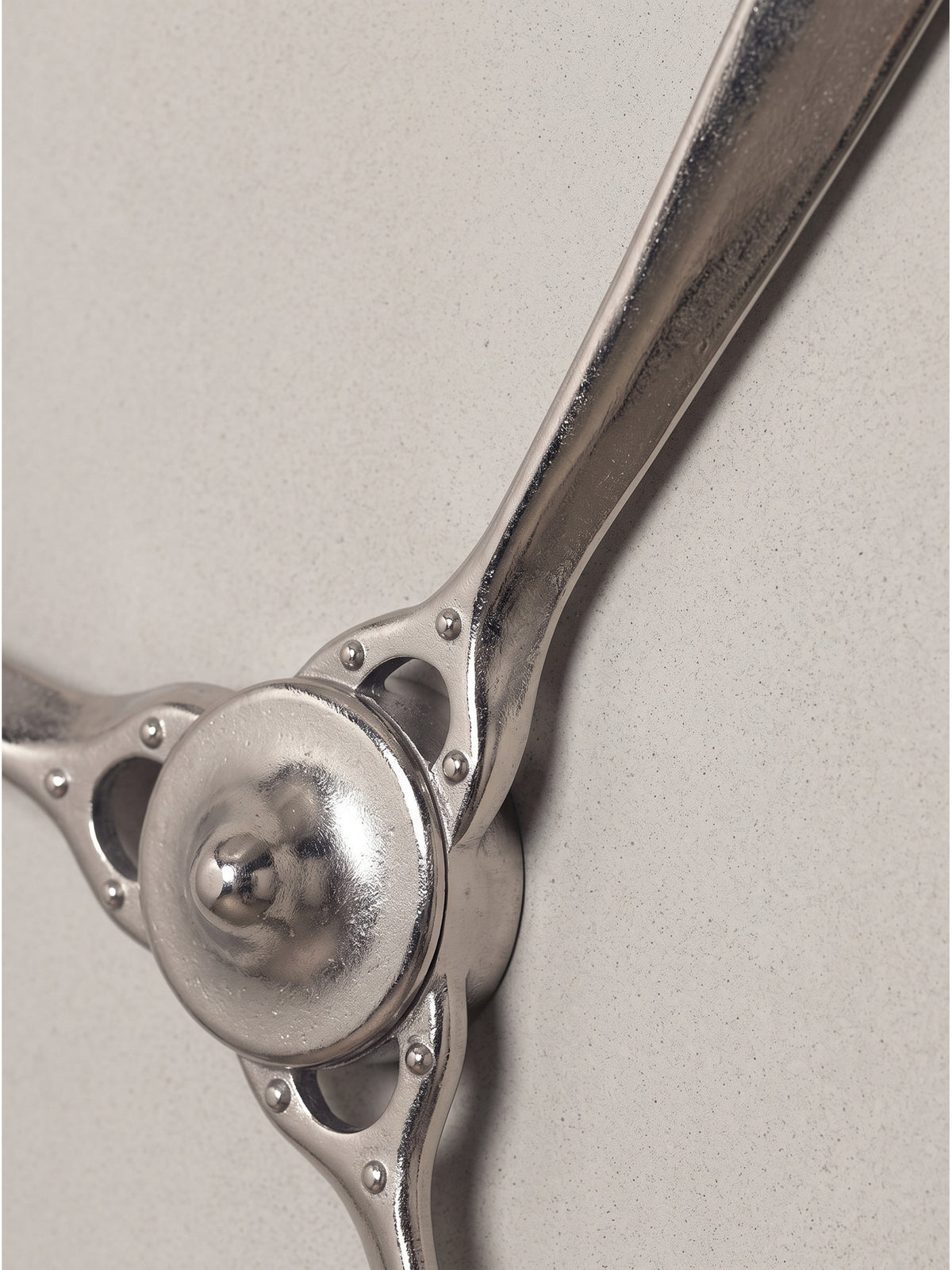 Makroaufnahme der runden Nabe des Wandpropellers aus vernickeltem Metall mit kreisförmigen Zierausschnitten und Schrauben.