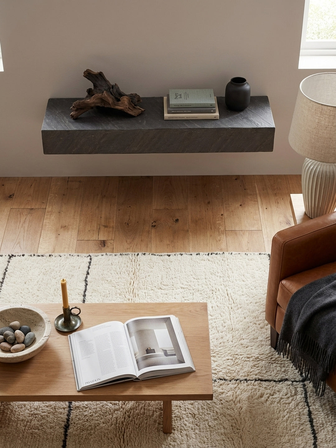 Draufsicht auf ein Wohnzimmer-Arrangement mit dem anthrazitfarbenen Schweberegal als Blickfang über einem minimalistischen Sideboard aus Holz._