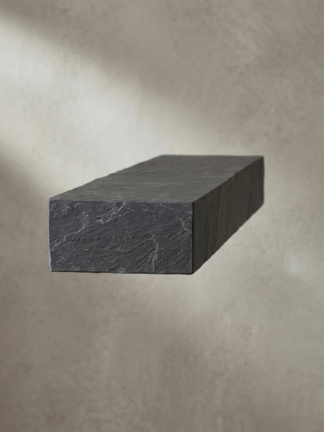 Eine alternative Perspektive auf das anthrazitfarbene Schweberegal, die das Lichtspiel auf der dreidimensionalen Steinoptik-Oberfläche betont._