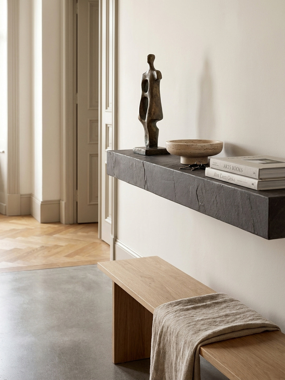 Das anthrazitfarbene Wandregal aus Mangoholz, dekoriert mit einer Bronzeskulptur und einer Travertinschale als elegante Ablage im modernen Flur._