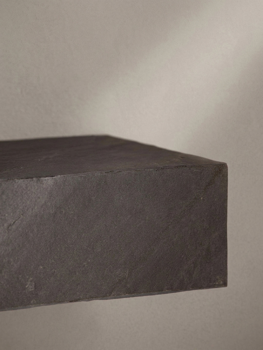 Nahaufnahme der Kantenverarbeitung des Wandregals, dessen Kunststoffoberfläche die charakteristischen Unregelmäßigkeiten von Stein imitiert._