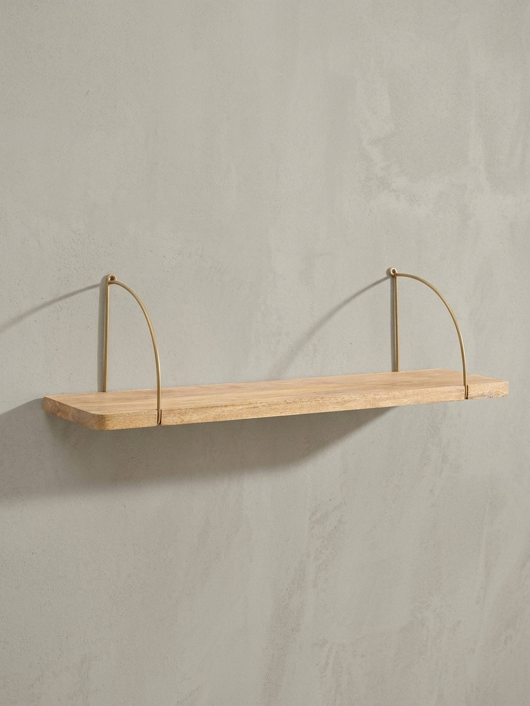 Design-Wandregal in 3/4-Ansicht, das die Tiefe der 22 cm Ablagefläche aus Mangoholz und die elegante Biegung der goldenen Halterungen hervorhebt._