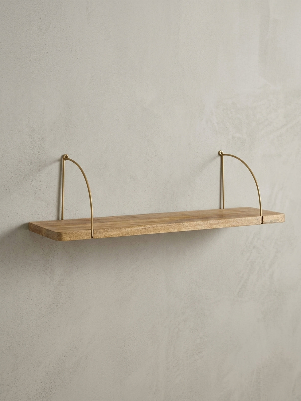 Design Schweberegal in der 3/4-Ansicht, die das Zusammenspiel von warmem Mangoholz und den filigranen Metallbügeln in Gold unterstreicht._