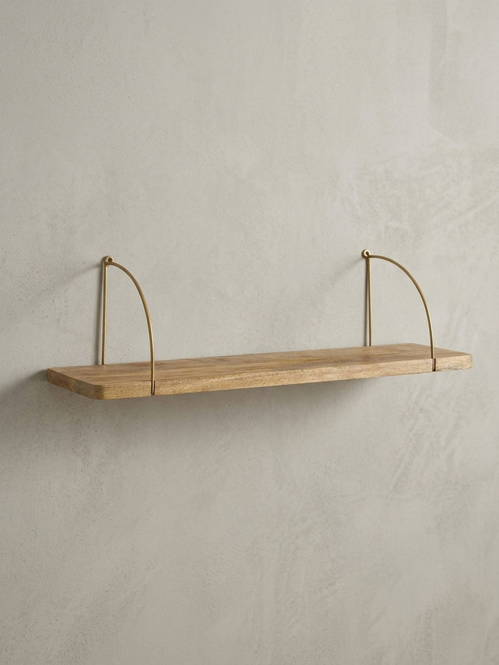Design Schweberegal in der 3/4-Ansicht, die das Zusammenspiel von warmem Mangoholz und den filigranen Metallbügeln in Gold unterstreicht._