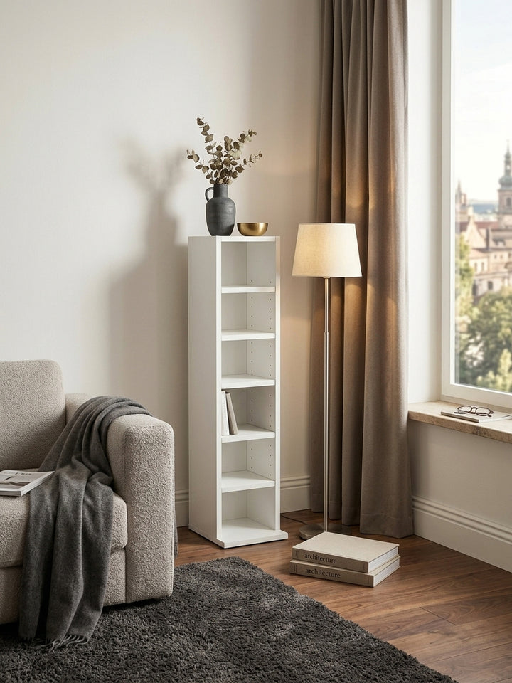 Draufsicht auf das kompakte Nischenregal in Weiß, 21x91x25,5 cm, platziert neben einem Designer-Sessel auf dunklem Walnuss-Parkettboden im Home Office._
