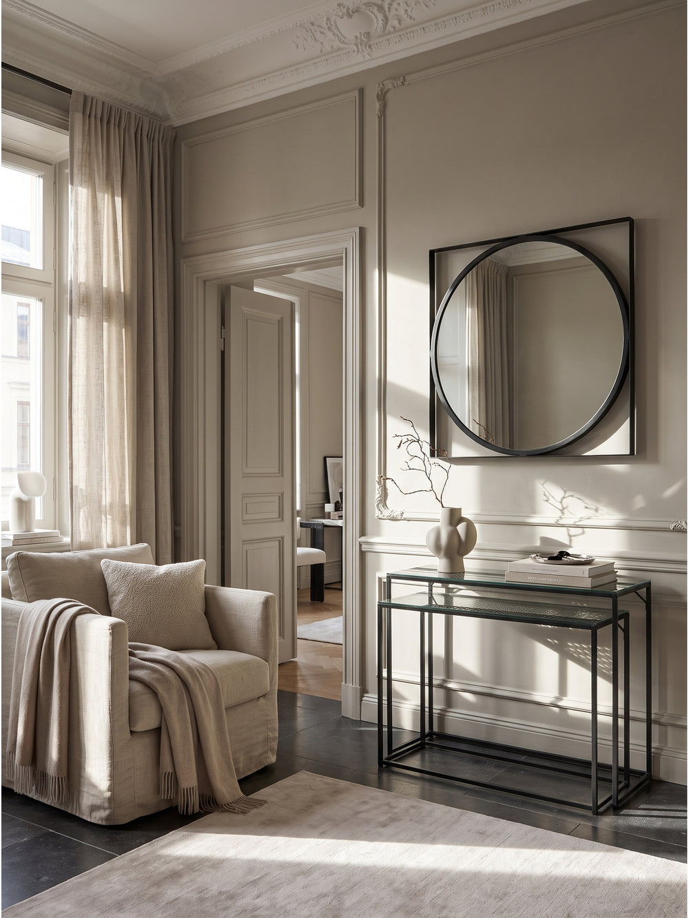 Eleganter Wandspiegel mit schwarzem Eisenrahmen 54x54 cm im luxuriösen Entrée über einer schwebenden Nussbaum-Konsole an einer greige gekalkten Wand._
