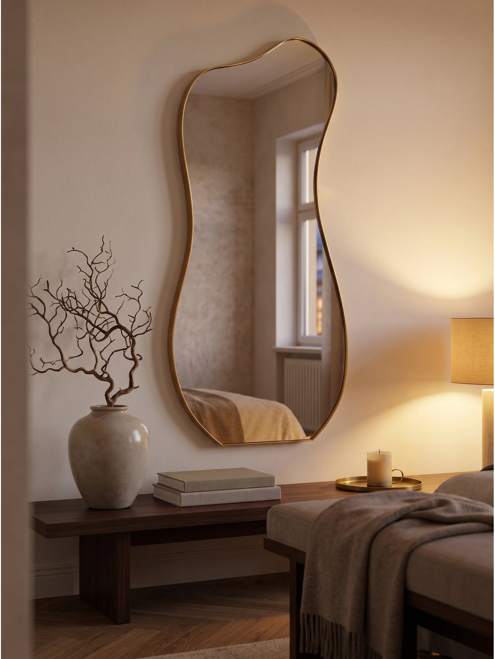 Eleganter Hängespiegel in Unform neben einer skulpturalen Keramikvase mit getrockneten Zweigen in einem hellen, eleganten Entrée._