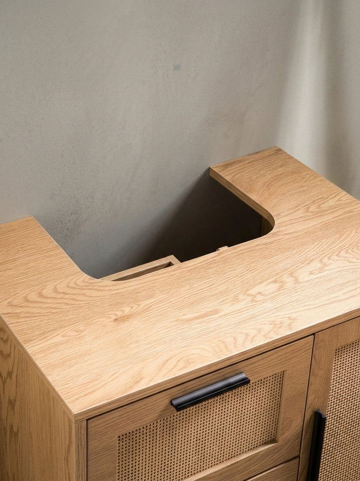 Nahaufnahme eines der schwarzen, minimalistischen Griffe am Waschtischunterschrank vor dem Hintergrund des beigefarbenen Rattangeflechts._