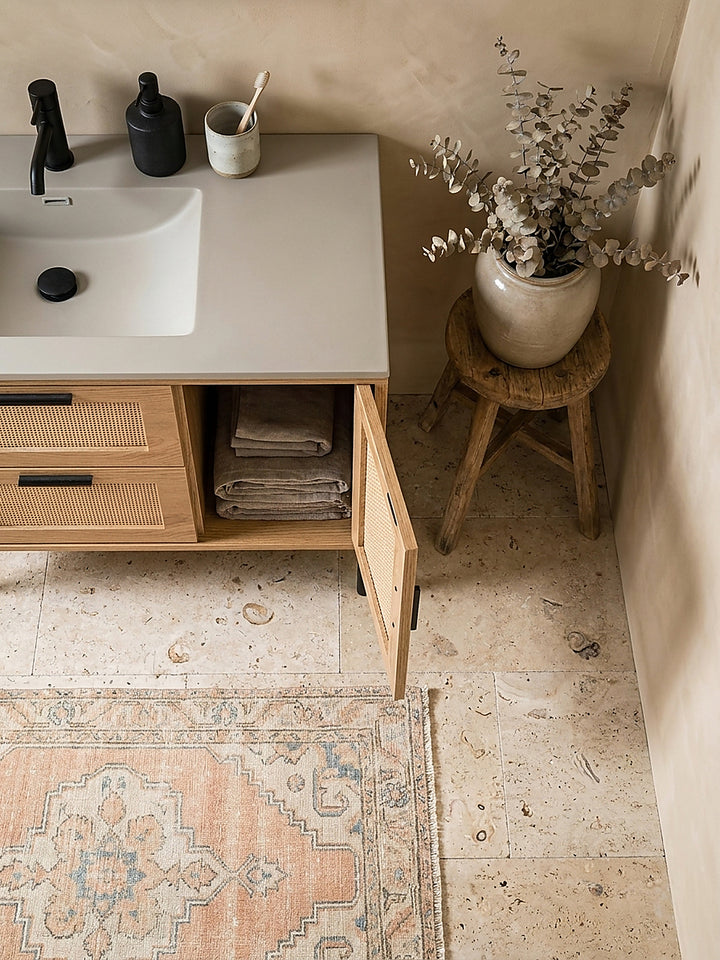 Aufsicht auf einen stehenden Badschrank 60x60 cm mit Wiener Geflecht, platziert auf einem runden Juteteppich vor einem modernen Waschtisch._