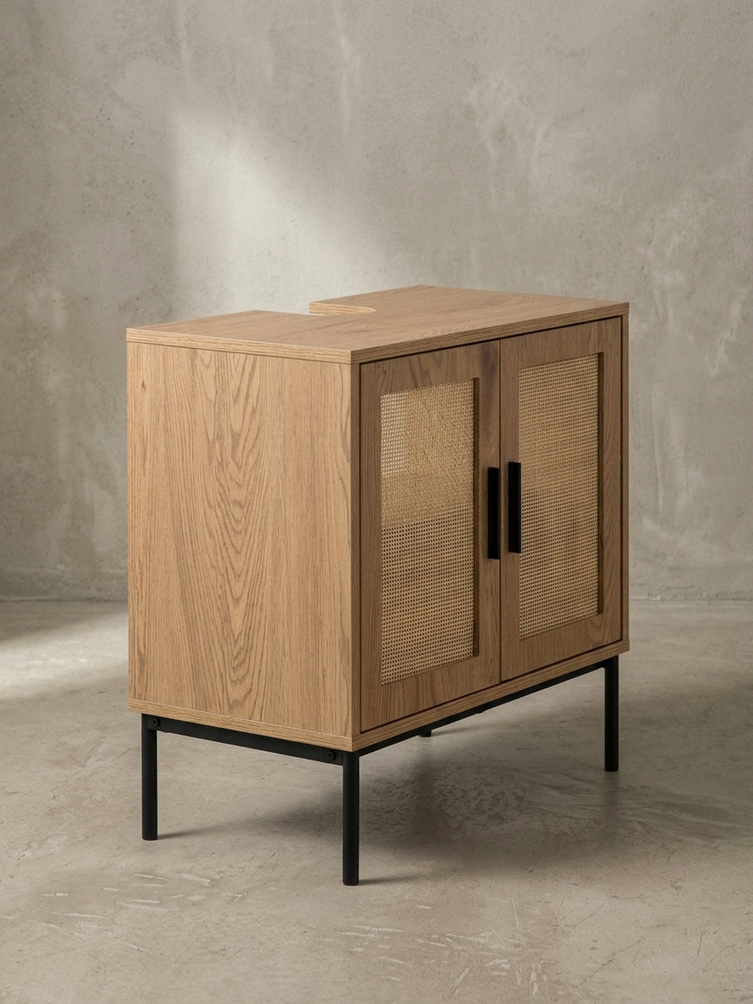 Detailaufnahme eines der vertikalen, mattschwarzen Griffe am Badezimmerschrank, montiert auf der Tür mit dem hellen Polyrattan-Geflecht._