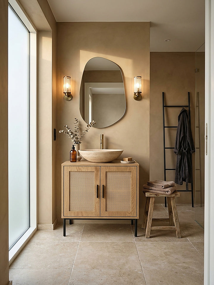 Eleganter Waschbeckenunterschrank in Eiche-Optik mit Polyrattan-Türen im organisch-modernen Spa-Badezimmer auf hellem Travertin-Boden unter einem Aufsatzwaschbecken._
