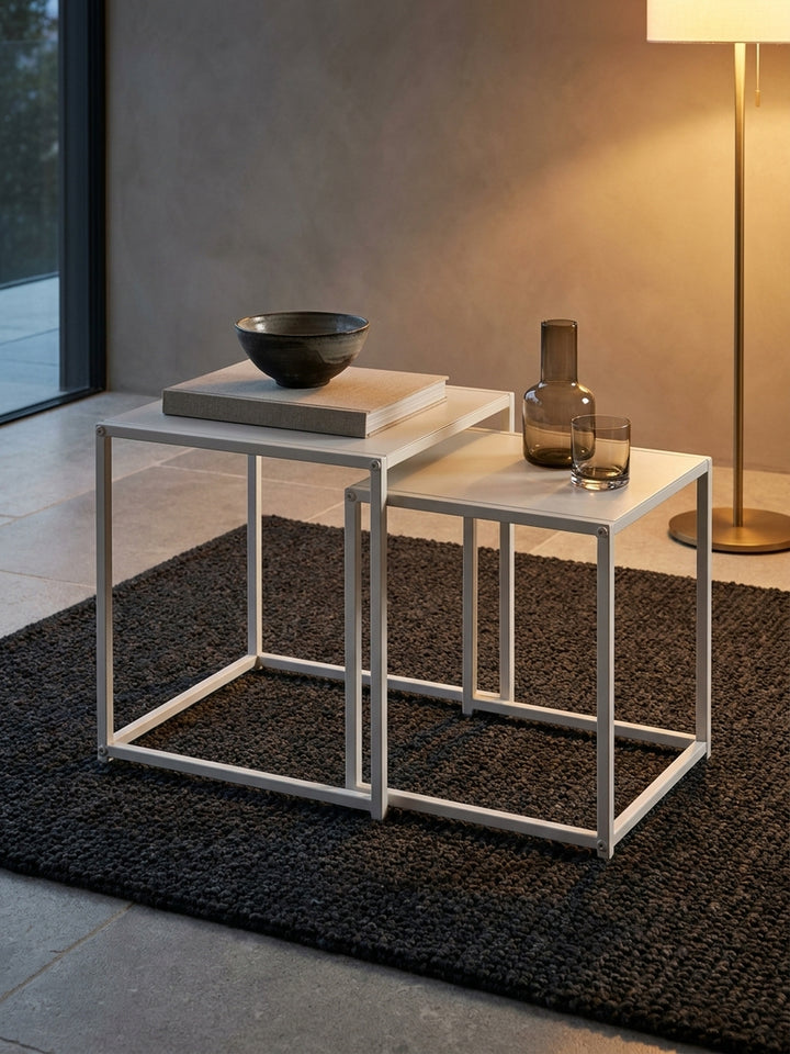 Gemütliches Styling mit einer schwarzen Teekanne und zwei Tassen auf dem größeren Sofatisch aus weißem Metallblech neben einem weichen hellgrauen Sofa._